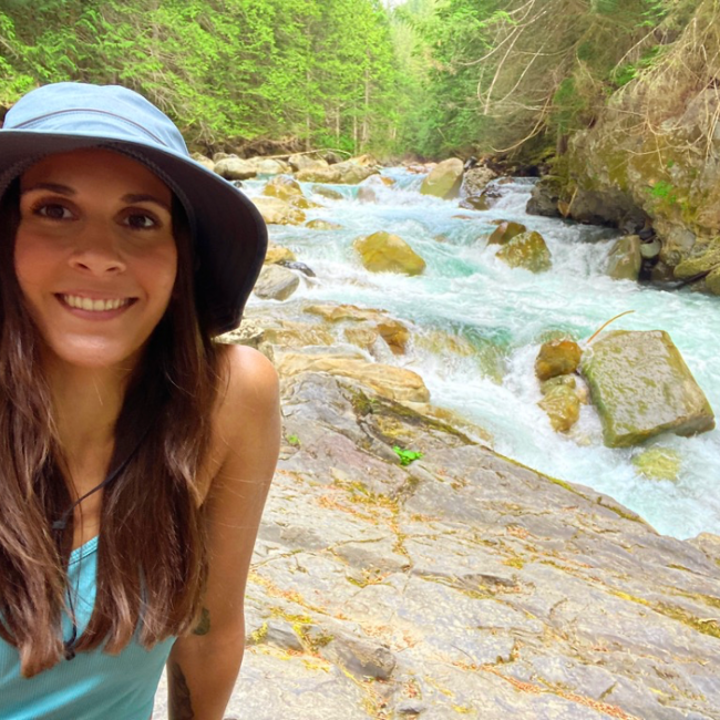 Kristin Carlson smiles at the camera as a glacier-fed waterfall roars behind her